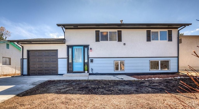 split level home with a garage, driveway, and stucco siding