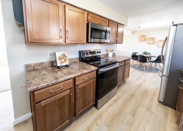 kitchen with a textured ceiling, light wood-style flooring, baseboards, appliances with stainless steel finishes, and brown cabinets