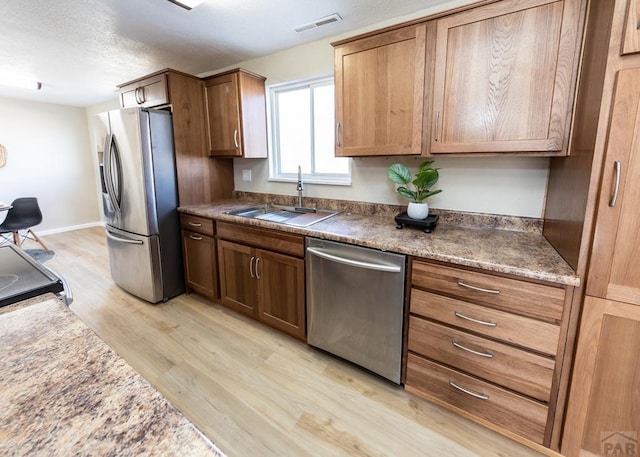 kitchen featuring a sink, visible vents, baseboards, light wood-style floors, and appliances with stainless steel finishes