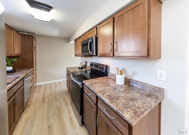 kitchen with stainless steel appliances, light wood finished floors, brown cabinetry, and baseboards