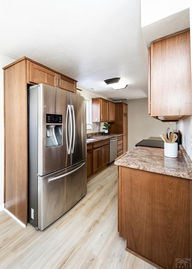 kitchen with light wood finished floors, stainless steel appliances, a textured ceiling, light countertops, and a sink