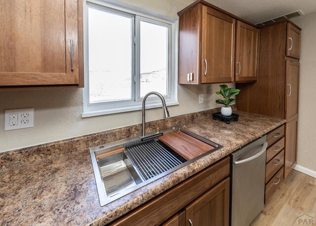 kitchen featuring light wood finished floors, visible vents, stainless steel dishwasher, brown cabinetry, and a sink