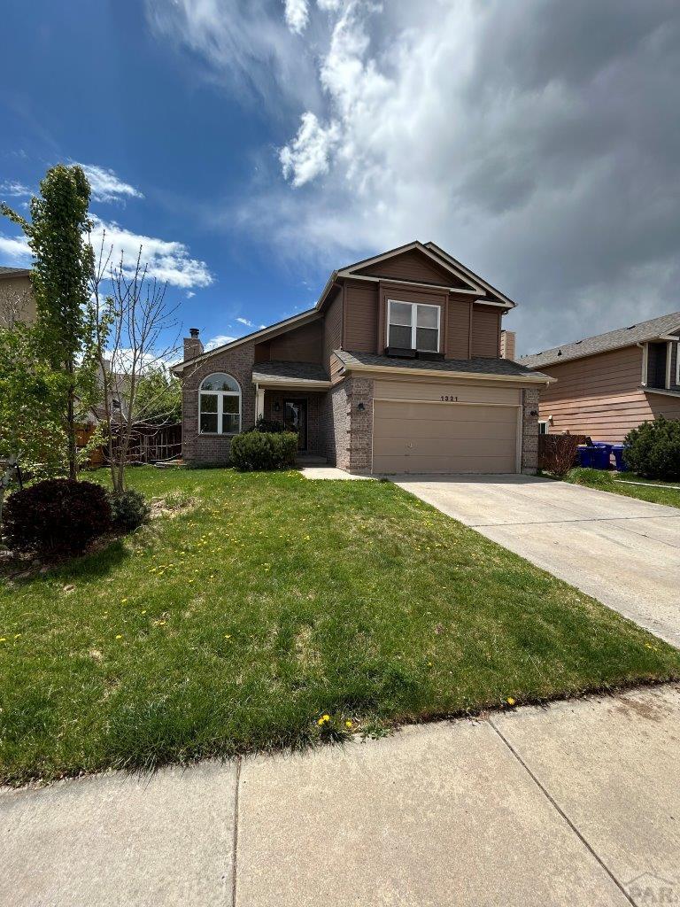 traditional home featuring brick siding, a garage, driveway, and a front yard
