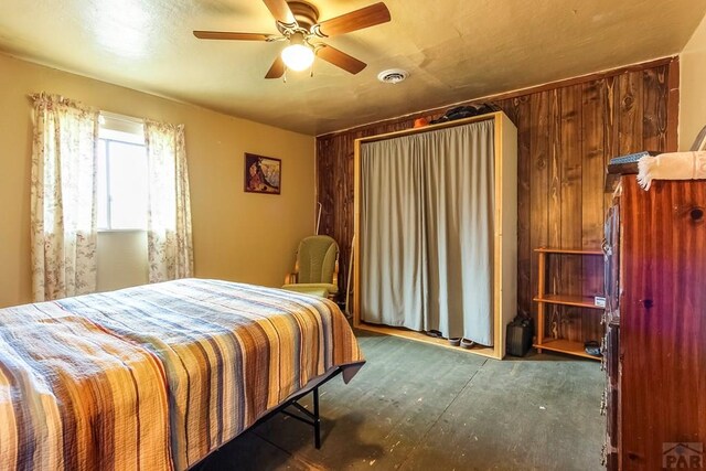 bedroom with wooden walls, visible vents, and a ceiling fan