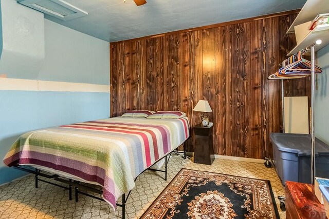 bedroom featuring attic access, wood walls, and a ceiling fan