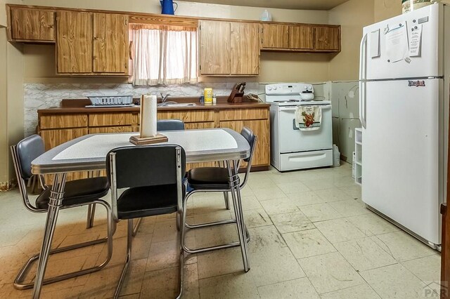 kitchen with white appliances, brown cabinets, a sink, and light floors