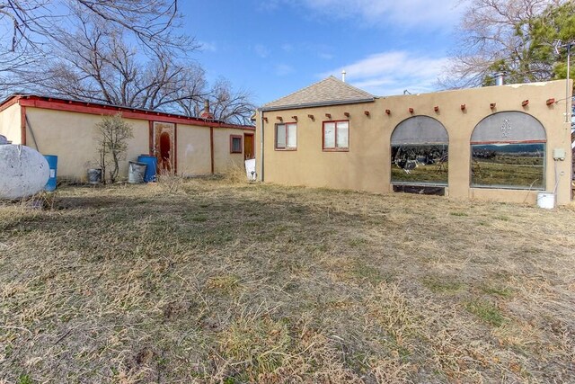 rear view of property featuring a shingled roof and stucco siding