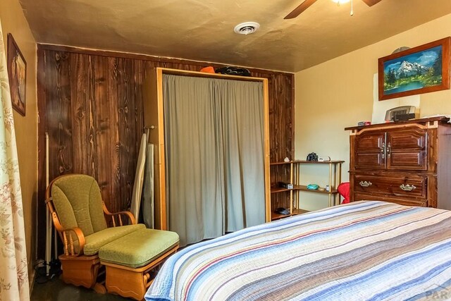 bedroom with wood walls, visible vents, and a ceiling fan