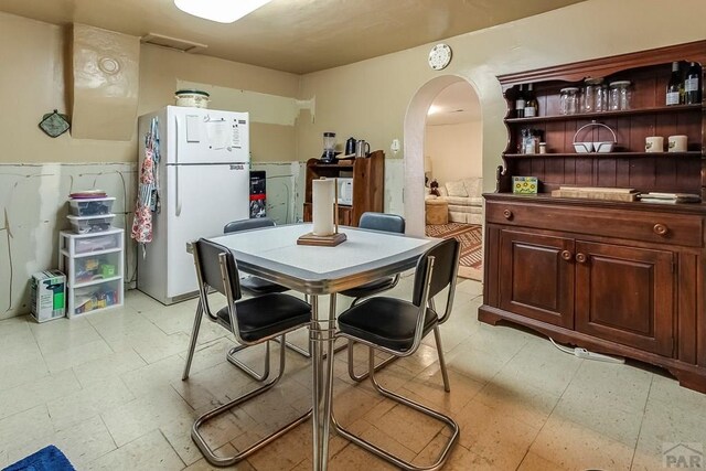 kitchen featuring arched walkways, open shelves, light floors, and freestanding refrigerator