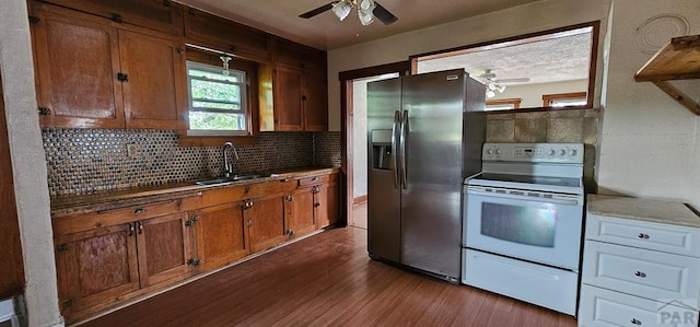 kitchen with stainless steel fridge, white range with electric stovetop, dark wood finished floors, brown cabinetry, and a sink