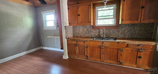 kitchen with brown cabinetry, a sink, backsplash, and baseboards