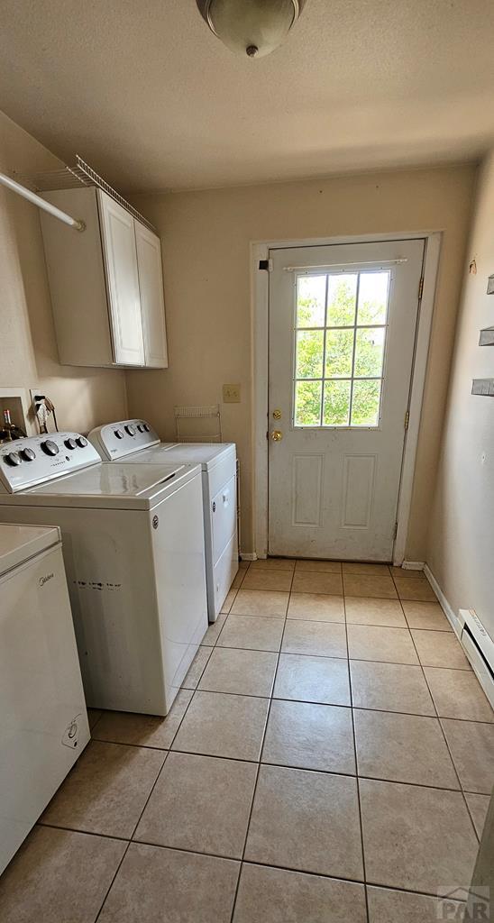 clothes washing area with a textured ceiling, light tile patterned flooring, baseboards, washer and dryer, and cabinet space