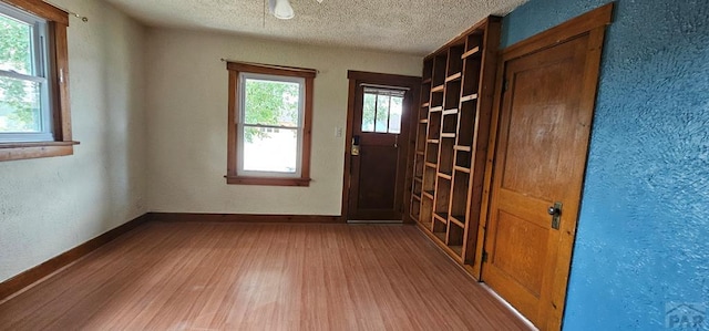 foyer entrance with a textured ceiling, baseboards, and wood finished floors