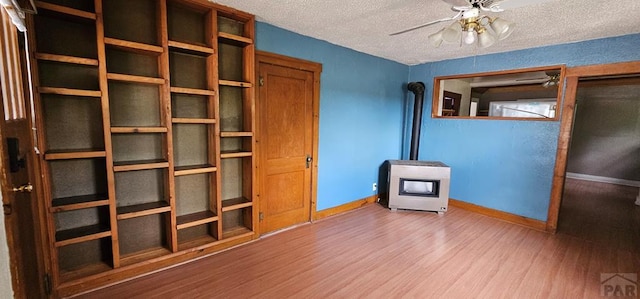 interior space with a wood stove, a textured ceiling, baseboards, and wood finished floors