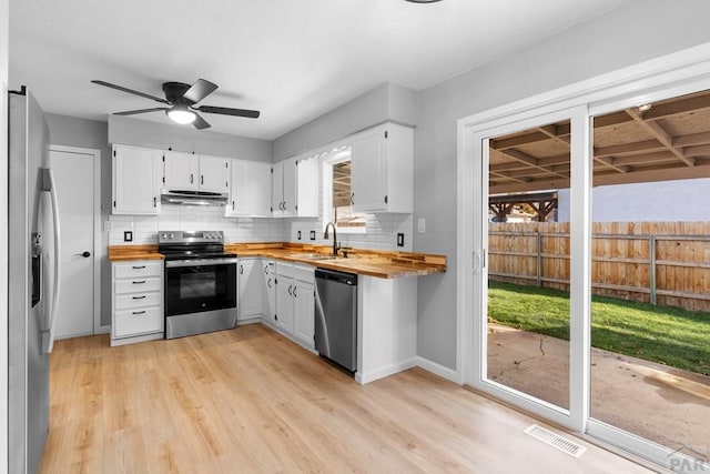 kitchen with butcher block countertops, appliances with stainless steel finishes, under cabinet range hood, white cabinetry, and a sink