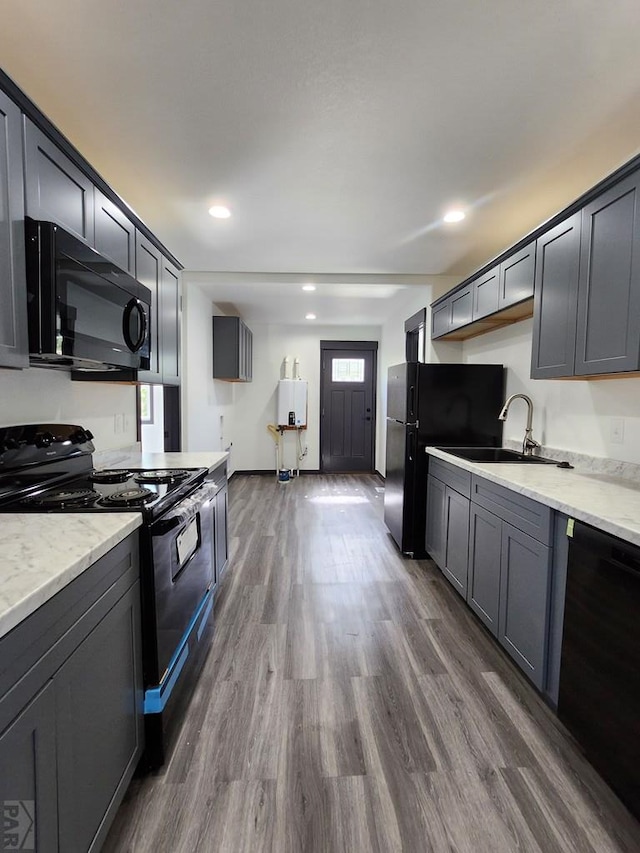 kitchen featuring dark wood-style flooring, recessed lighting, a sink, light stone countertops, and black appliances