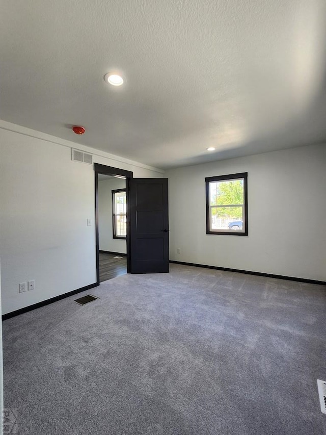 unfurnished room with visible vents, dark colored carpet, and a wealth of natural light