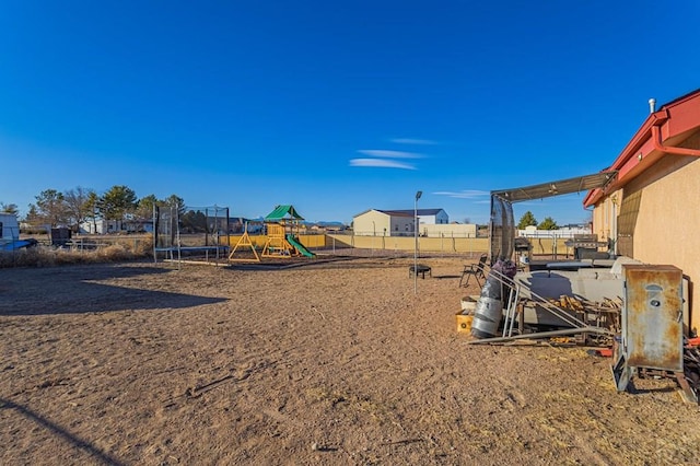 view of yard featuring a trampoline, fence, and playground community