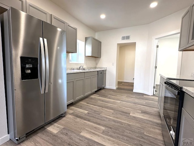 kitchen featuring visible vents, gray cabinets, a sink, stainless steel appliances, and light wood-style floors