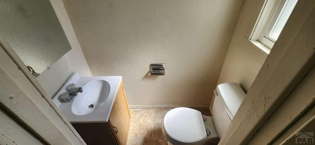 half bathroom with toilet, baseboards, a textured wall, and vanity