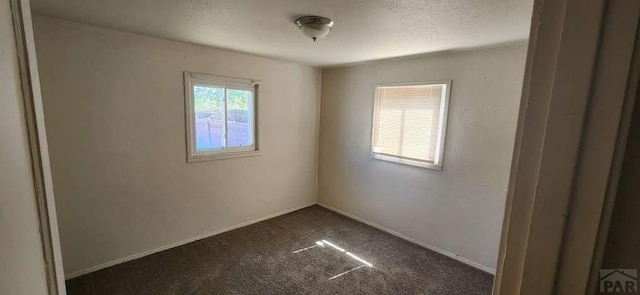spare room with baseboards, a textured ceiling, and dark carpet