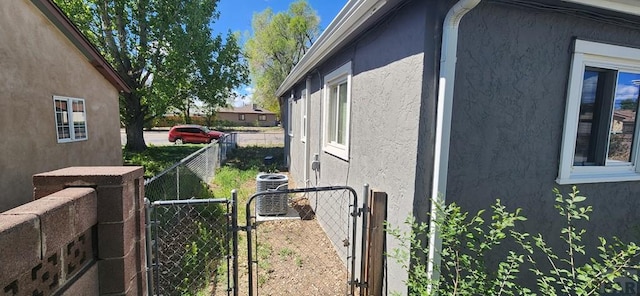view of side of home with central AC, a gate, and stucco siding