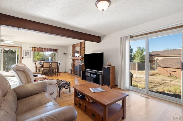 living room featuring light wood-style floors, visible vents, beamed ceiling, and a textured ceiling