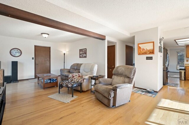 living room with a textured ceiling, light wood finished floors, and beamed ceiling