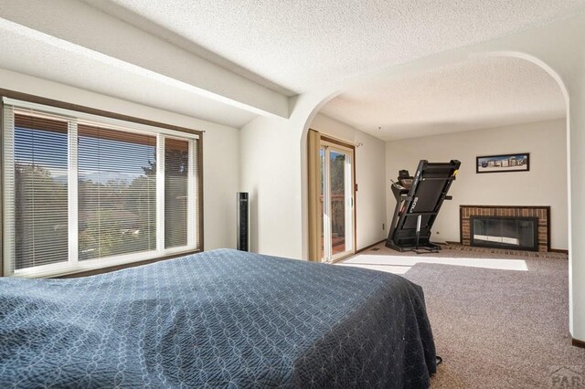 carpeted bedroom with arched walkways, a textured ceiling, and a brick fireplace