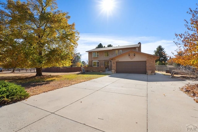 traditional-style home with driveway, a chimney, an attached garage, fence, and brick siding