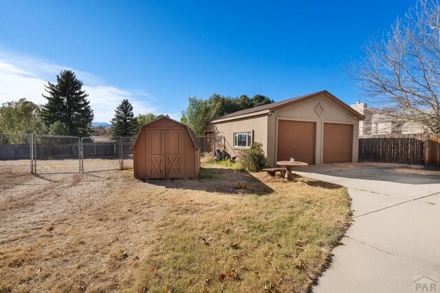 view of front of house featuring stucco siding, a detached garage, fence, and an outdoor structure