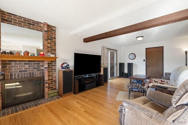 living area with a textured ceiling, a brick fireplace, wood finished floors, and beam ceiling