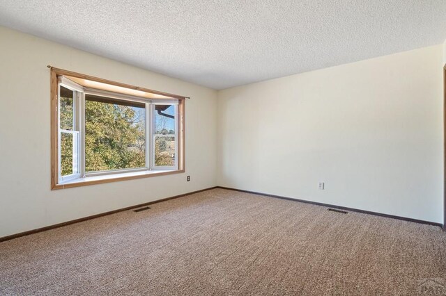 carpeted spare room featuring visible vents, a textured ceiling, and baseboards