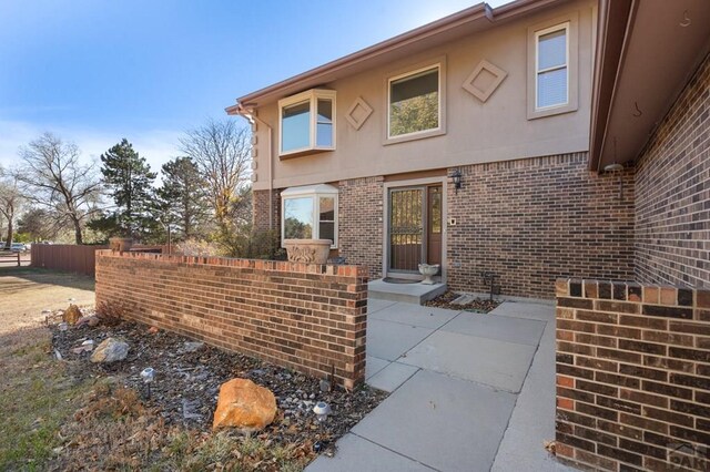 view of exterior entry featuring brick siding, a patio area, fence, and stucco siding