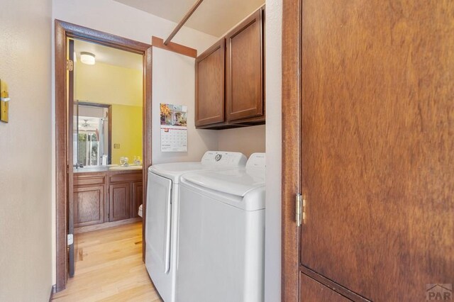 clothes washing area featuring separate washer and dryer, light wood-style flooring, a sink, and cabinet space