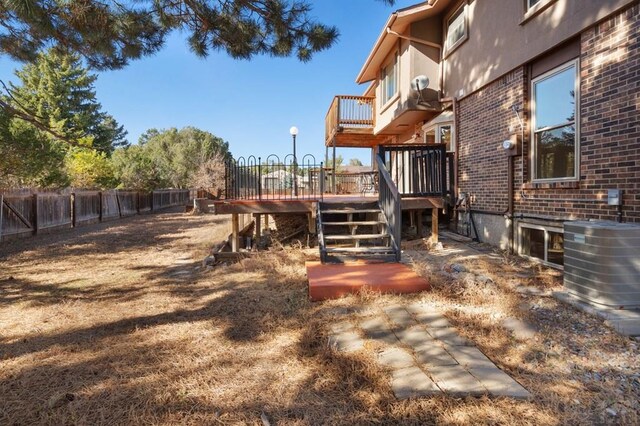 view of yard with fence, central AC unit, a wooden deck, and stairs