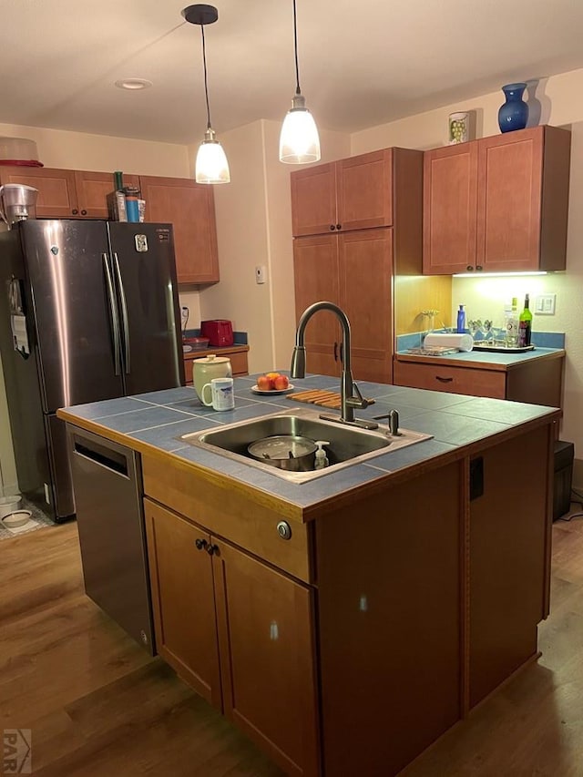 kitchen with stainless steel appliances, brown cabinetry, a sink, and a center island with sink