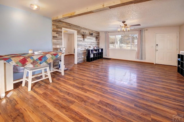 living room featuring a textured ceiling, ceiling fan, wood walls, wood finished floors, and baseboards