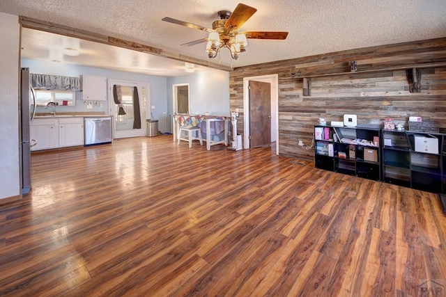 unfurnished living room featuring a ceiling fan, wood finished floors, a textured ceiling, wood walls, and a sink