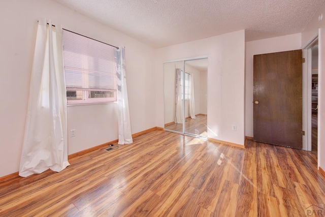 unfurnished bedroom featuring a textured ceiling, light wood finished floors, a closet, and baseboards