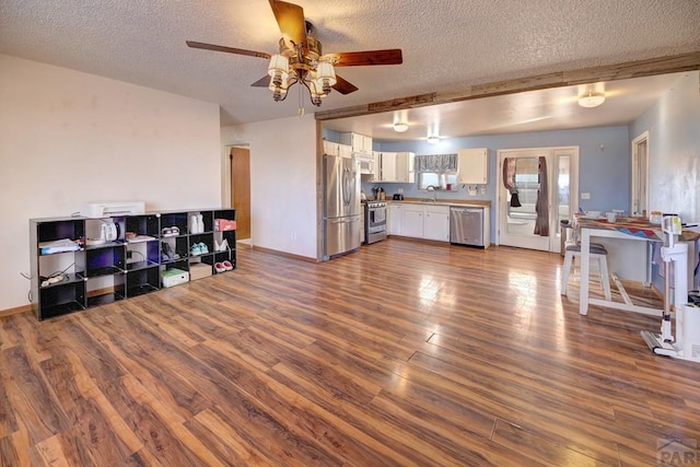 interior space with dark wood finished floors, stainless steel appliances, a textured ceiling, white cabinetry, and a sink