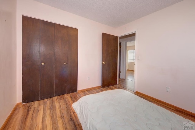 bedroom featuring light wood finished floors, a closet, baseboards, and a textured ceiling