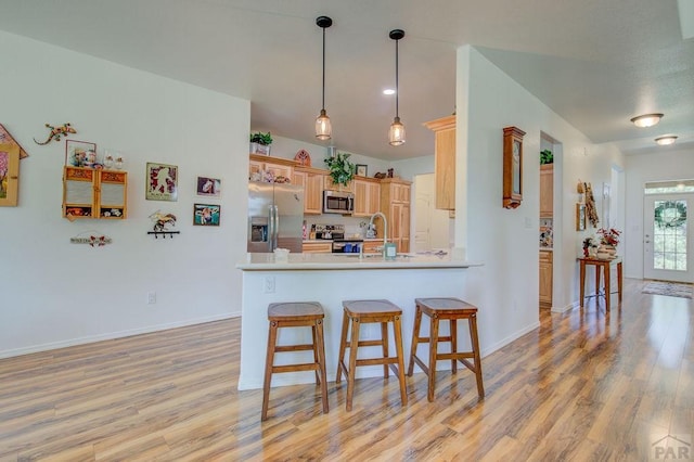 kitchen featuring light wood-type flooring, a peninsula, appliances with stainless steel finishes, and a kitchen breakfast bar