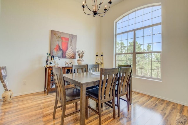 dining space featuring light wood-type flooring, a high ceiling, baseboards, and a notable chandelier