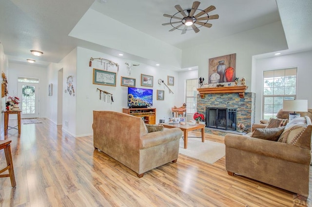 living area with light wood-style flooring, baseboards, a ceiling fan, and a stone fireplace