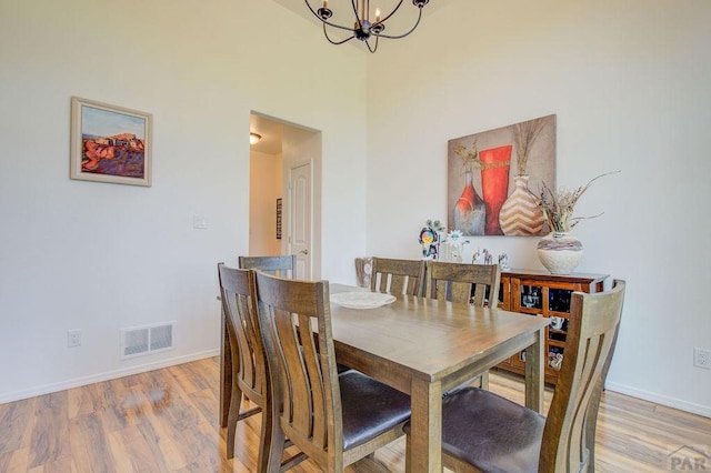 dining room with light wood-type flooring, baseboards, visible vents, and a notable chandelier