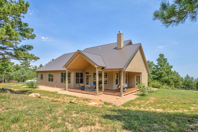 rear view of property featuring a yard, a chimney, stucco siding, metal roof, and a wooden deck