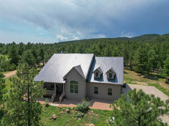 rear view of house with metal roof, stucco siding, and a view of trees