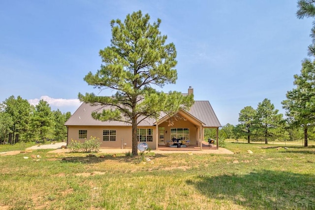 back of property with a standing seam roof, metal roof, a yard, a chimney, and a patio area