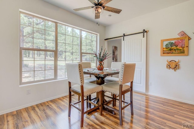 dining room with light wood-type flooring, a barn door, baseboards, and a ceiling fan